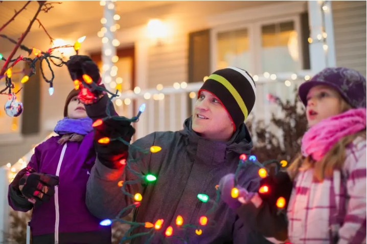 A family untangling a string of Christmas lights on their porch.
